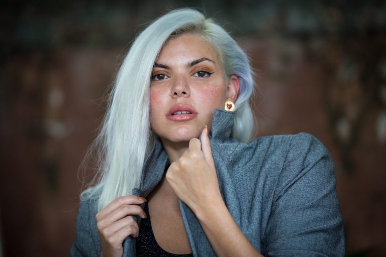 Duda Beat posa para a foto, com uma jaqueta azul e brincos dourados