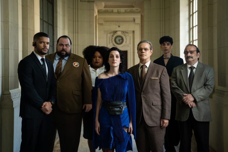 Cena oficial da série Eleita, com Clarice Falcão no centro, usando roupa azul, e um grupo de pessoas ao redor