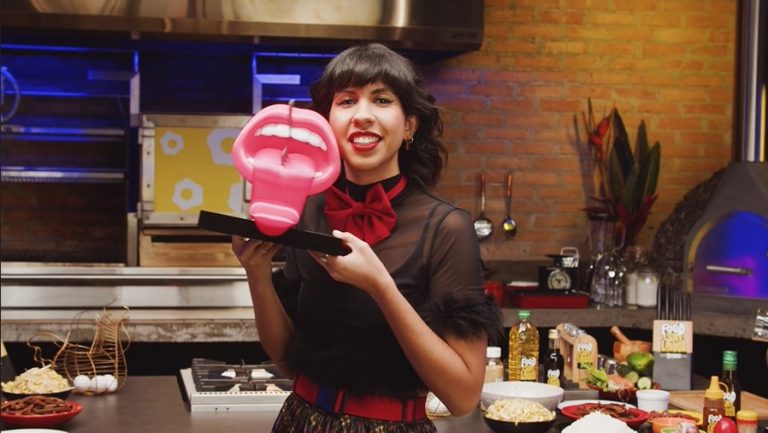 Foto oficial da divulgação do programa Food Is My Língua. Apresentadora posa para a foto segurando o troféu da disputa