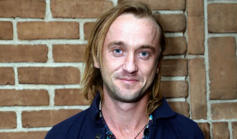 Tom Felton posa para a foto em frente a parede de tijolos