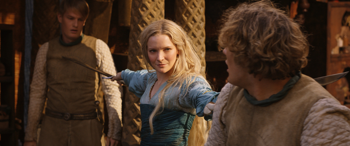 A atriz Morfydd Clark, branca e loira, empunha duas espadas contra dois homens, em cena, como Galadriel em Senhor dos Anéis: Os Anéis do Poder.