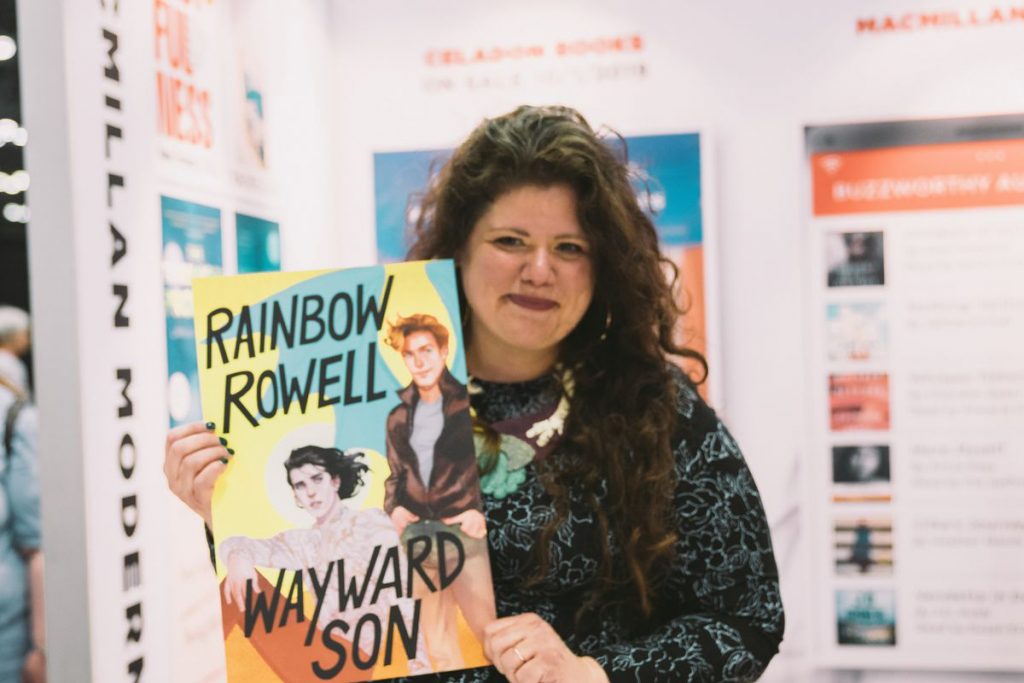 Rainbow Rowell segura o pôster da capa de um de seus livros da série de Simon Snow