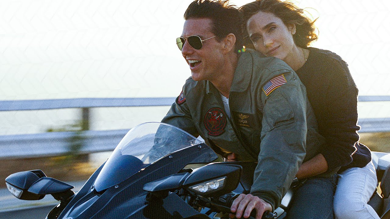 O ator Tom Cruise dirige uma moto e a atriz Jennifer Connelly aparece ao fundo, na garupa, em cena em "Top Gun: Maverick".