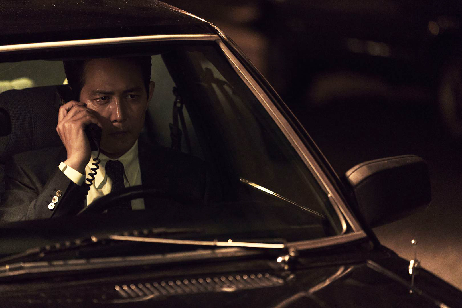 Lee Jung Jae fala ao telefone dentro de um carro, durante seu processo de espionagem no filme Operação Hunt, que estreia em fevereiro