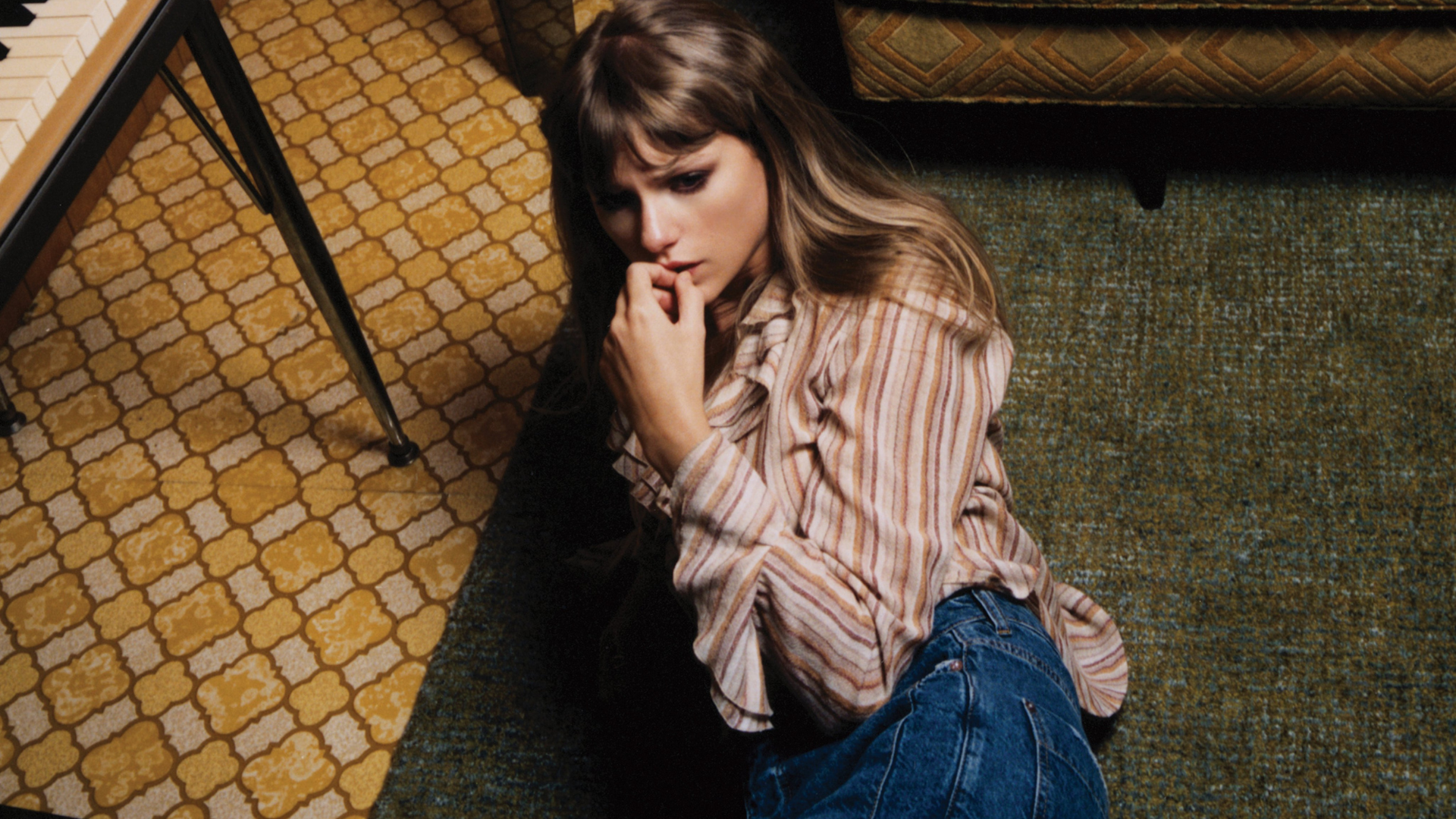 Taylor Swift sentada no chão, em um tapete, com cara de preocupada. Foto presente na sessão de fotos feita para o álbum Midnights