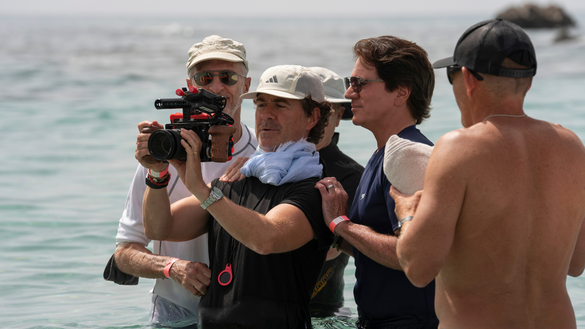 Foto dos bastidores das gravações de A Pequena Sereia. Na imagem há 4 homens no mar e um deles está segurando uma câmera, filmando uma cena